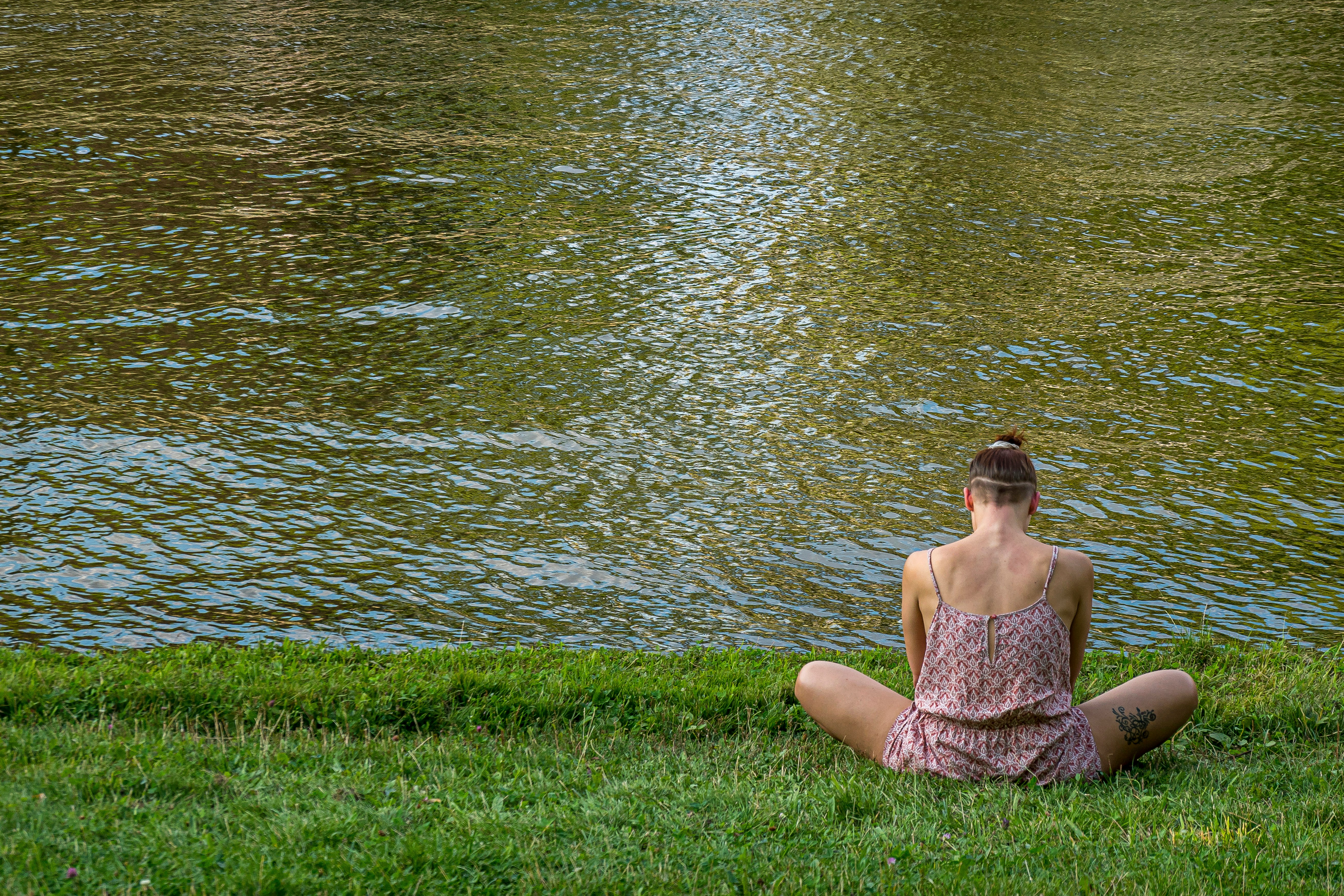 woman in brown tube dress sitting on green grass field near body of water during daytime